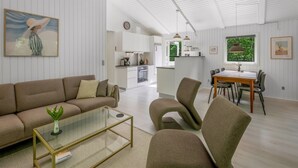 Een moderne woonkamer met een bank, salontafel en stoelen, een eethoek met een tafel en stoelen, en een keuken op de achtergrond.