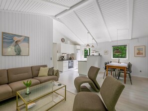 Un salon moderne avec un canapé, une table basse et des fauteuils, un coin repas avec une table et des chaises, et une cuisine en arrière-plan.