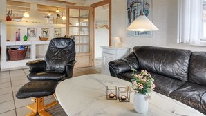 En moderne stue med en sort lædersofa, en matchende lænestol og et marmorbord. Der står en lille vase med blomster på bordet.