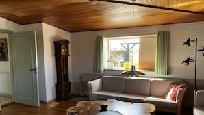 Una sala de estar acogedora con techo de madera, un sofá, una mesa de centro y un amplio ventanal con cortinas.