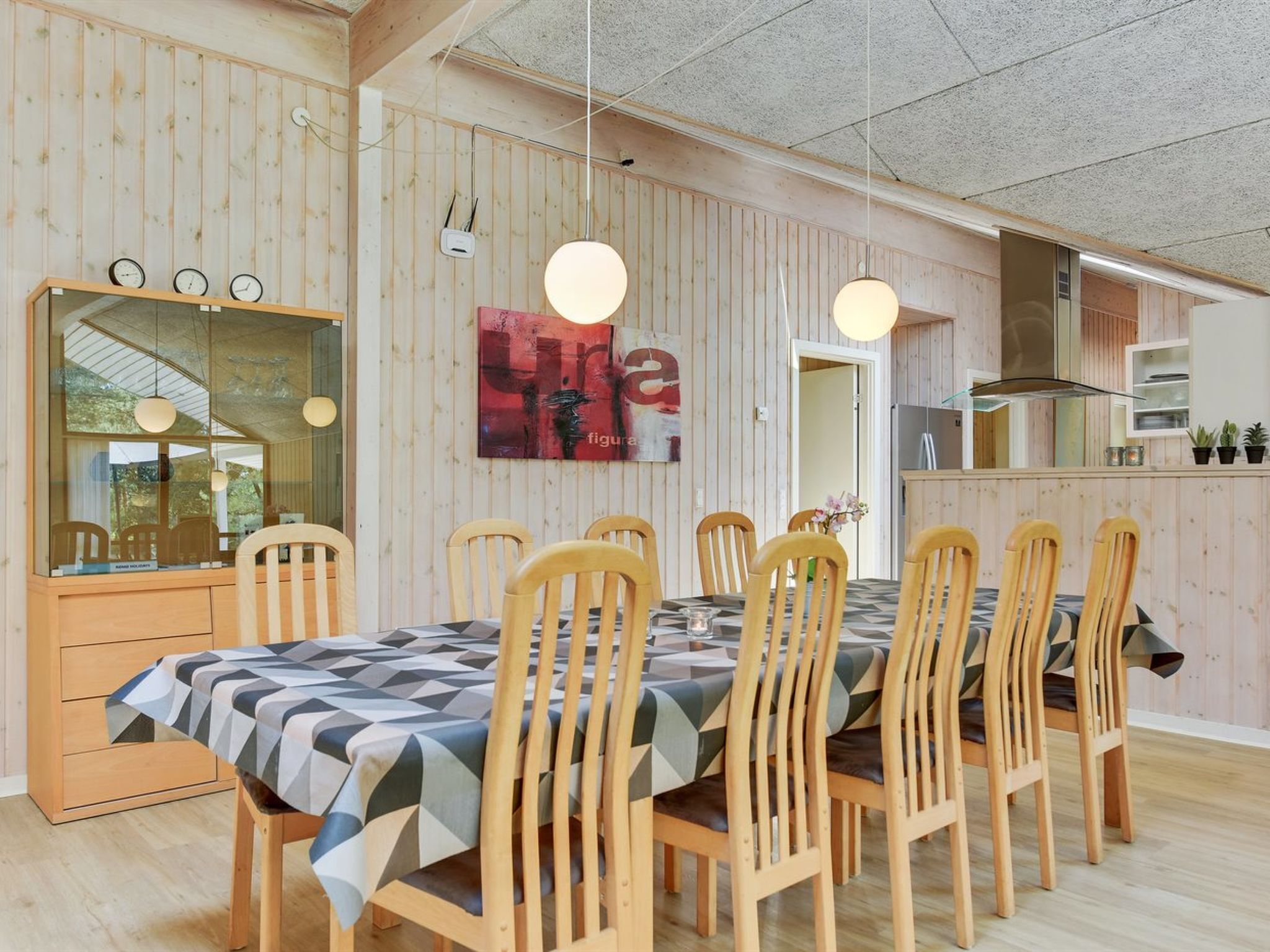 Un comedor con una mesa y sillas de madera, un espejo grande y una cocina al fondo.