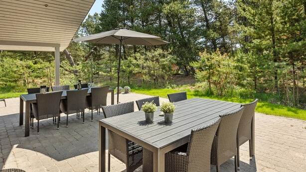 An outdoor patio with a covered table and chairs, surrounded by a wooded area.