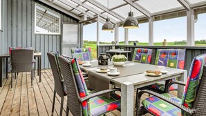 A covered patio with a table and chairs, large windows, and a view of the countryside.