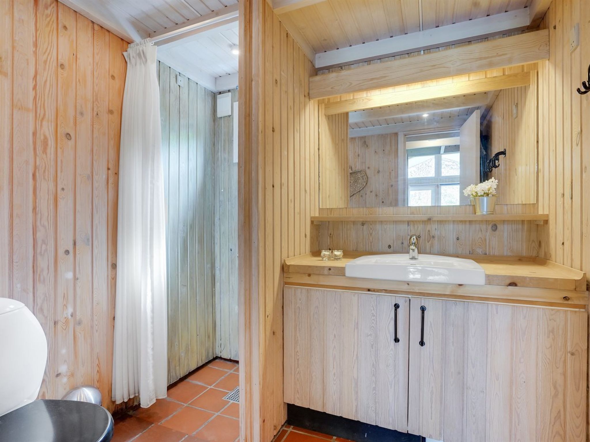 Un baño de madera con lavamanos blanco, un espejo y una zona de ducha.