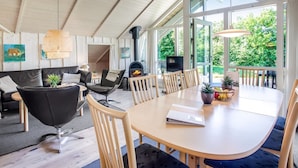 Un salon moderne doté d’une cheminée, d’un coin repas et de grandes fenêtres offrant une vue sur la verdure.