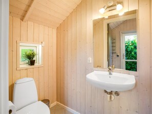 Ein Badezimmer mit Holzwandverkleidung, einer weißen Toilette, einem Waschbecken mit goldfarbenem Wasserhahn und einem Spiegel darüber.