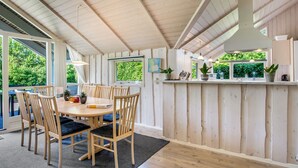 Un coin repas avec une table et des chaises en bois, un comptoir de cuisine agrémenté de plantes et de grandes fenêtres donnant sur un espace verdoyant.