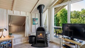 Un salon chaleureux avec un poêle à bois, un téléviseur à écran plat et une grande fenêtre donnant sur un paysage verdoyant.