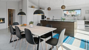 Een moderne keuken met een centraal eiland, hangende verlichting en een eethoek met een houten tafel en stoelen.
