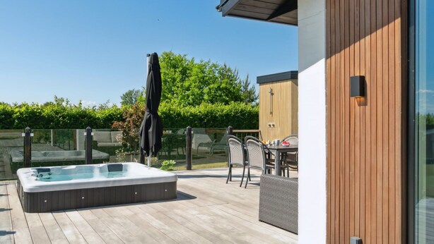Een houten terras met een jacuzzi, tuinmeubels en een glazen deur.