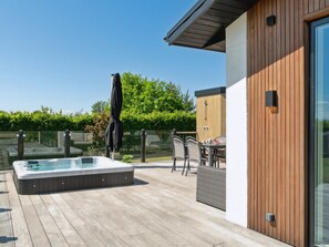 Une terrasse en bois avec un jacuzzi, du mobilier d’extérieur et une porte vitrée.