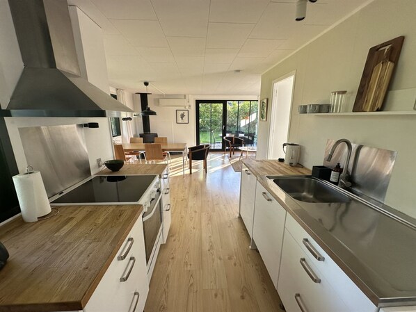 A modern kitchen with stainless steel appliances, wooden flooring, and a large window overlooking a garden.