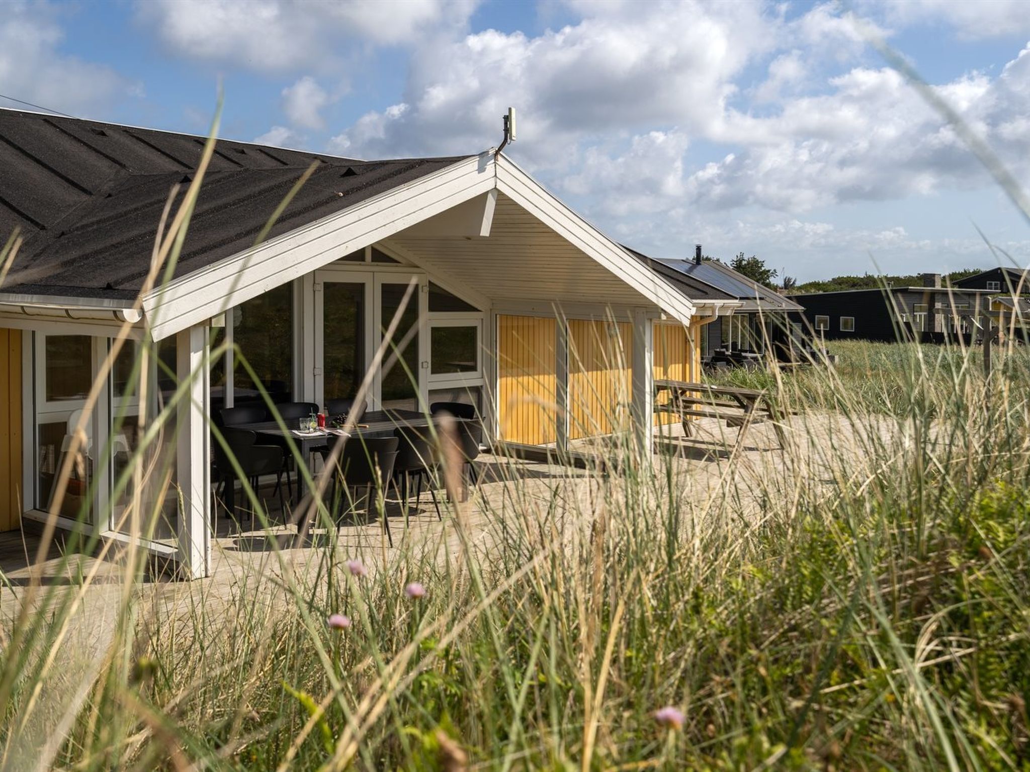 Ein modernes Haus mit einem geneigten Dach, großen Fenstern und einem überdachten Außenbereich mit Tisch und Stühlen.