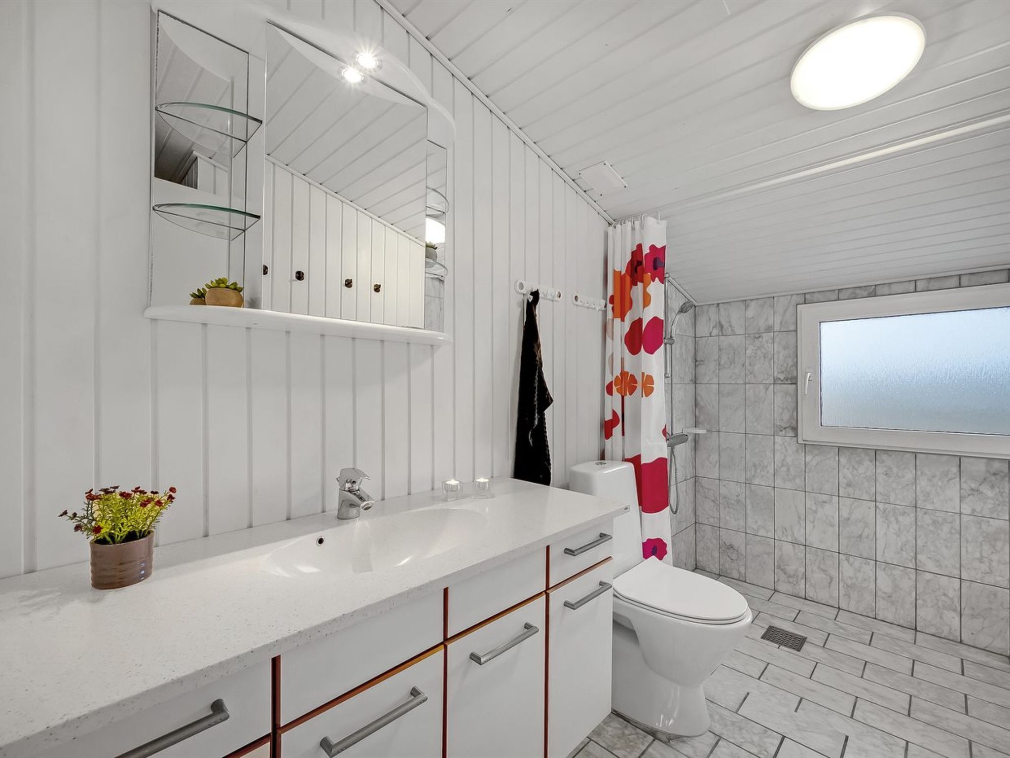 A modern bathroom with a white vanity, a large mirror, a shower with a glass door, and a toilet.