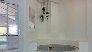 A bathroom with a large bathtub, a glass door, and hanging plants. - "Sirka" - 200m from the sea by Interhome (Vejers Strand)
