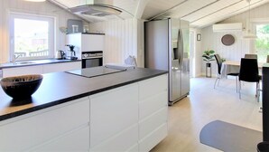 A modern kitchen with white cabinetry, a large island, stainless steel appliances, and a dining area with a table and chairs. - "Sirka" - 200m from the sea by Interhome (Vejers Strand)