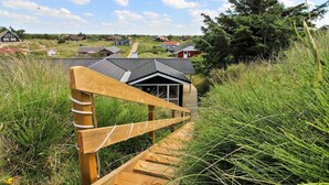 A wooden staircase leading to a building with a dark roof, surrounded by tall grass and a clear sky. - "Sirka" - 200m from the sea by Interhome (Vejers Strand)