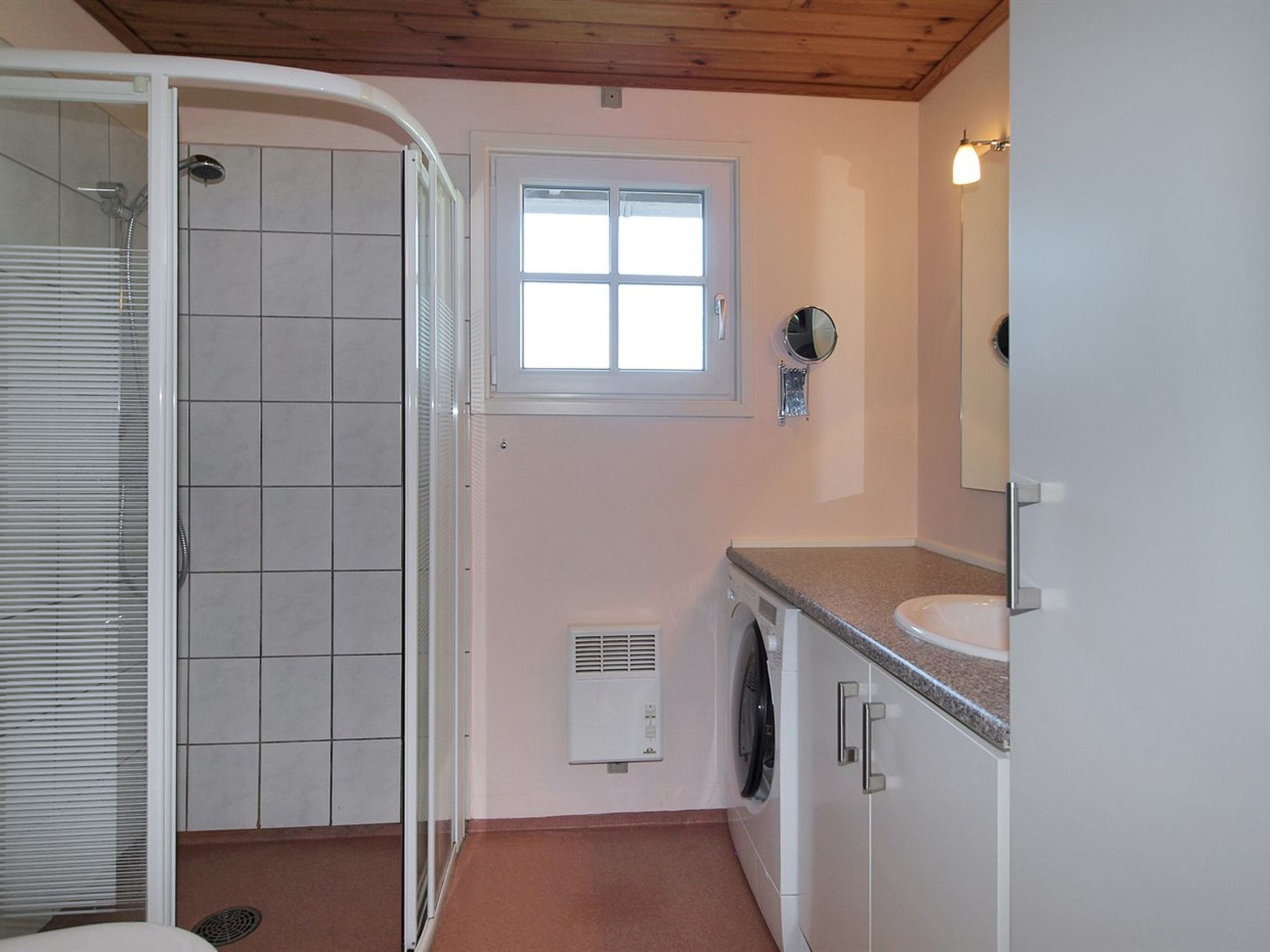 A bathroom with a shower, a window, a sink, and a mirror.