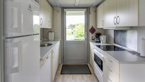 Cocina compacta con armarios blancos, horno empotrado, cafetera y ventana con vistas a la vegetación.