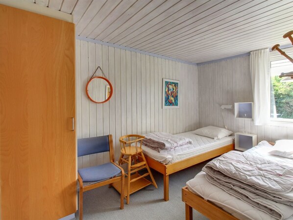 A dorm-style room with two beds, a chair, a desk, a mirror, and a window with curtains.