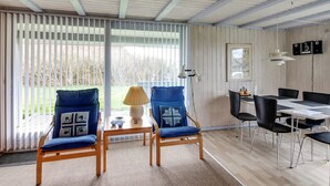 Una habitación con dos sillas azules, una mesa de madera, una lámpara y un comedor con una mesa y sillas.