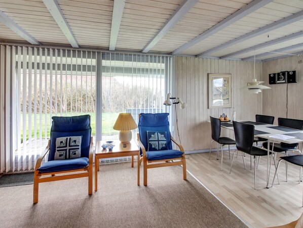 A room with two blue chairs, a wooden table, a lamp, and a dining area with a table and chairs.