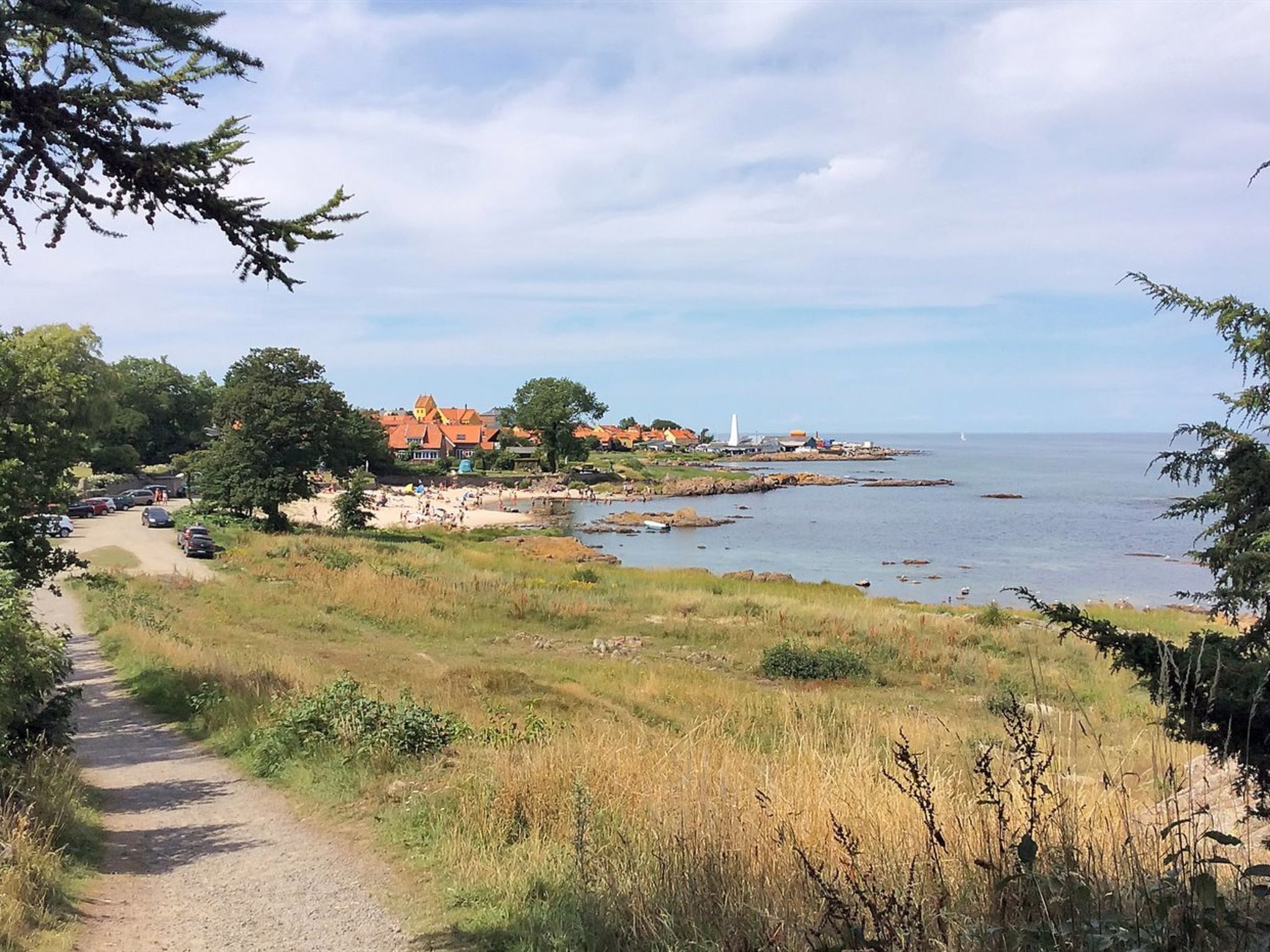 A coastal path leading to a beach with houses and a lighthouse in the background.