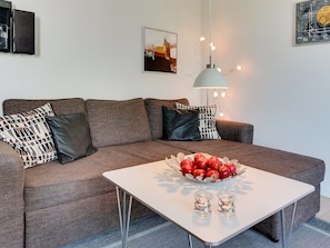 Ein modernes Wohnzimmer mit einem grauen Sofa, einem weißen Couchtisch und einer Schüssel mit Äpfeln.