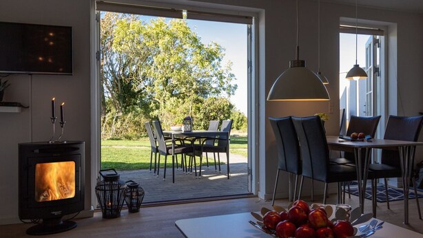 Eine moderne Küche mit Kaminofen, einem Essbereich mit Tisch und Stühlen sowie einem großen Fenster mit Blick auf einen Garten.