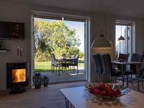 Een moderne keuken met een houtgestookte kachel, een eethoek met een tafel en stoelen, en een groot raam met uitzicht op een tuin.