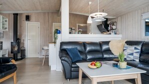 A modern living room with a black leather sofa, a wooden coffee table with fruit, and a kitchen in the background.