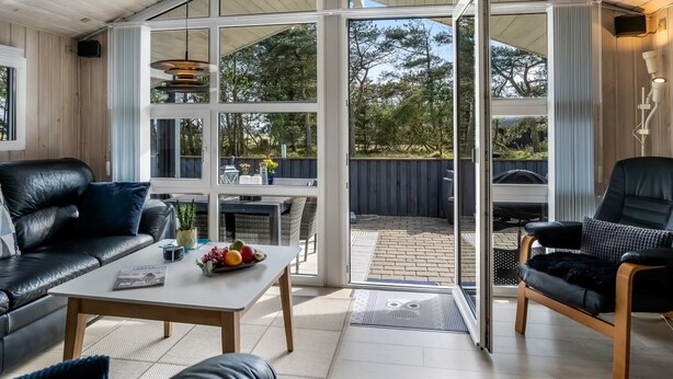 A modern interior with a glass door leading to an outdoor patio, a leather sofa, a coffee table with fruit, and a lamp.