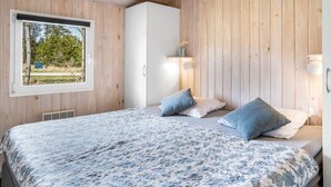A bedroom with a bed, wooden walls, a window, and a white wardrobe.