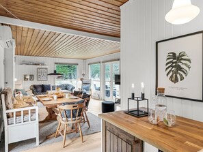 A spacious living area with a wooden ceiling, a dining table with chairs, a sofa, and a TV. There is a framed artwork on the wall and a window providing a view of greenery outside. - "Magrete" - 900m from the sea by Interhome (Blåvand)