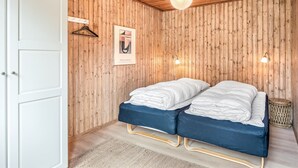 Une pièce aux murs recouverts de lambris en bois, un lit avec une literie bleue, un luminaire suspendu et un tableau encadré accroché au mur.