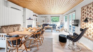 Un vaste espace de vie doté d’un plafond en bois, d’une table à manger avec des chaises, d’un canapé, d’une table basse et d’un téléviseur fixé au mur.