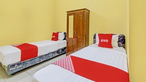 Dos camas individuales con ropa de cama roja y blanca, un armario de madera y una pared amarilla.