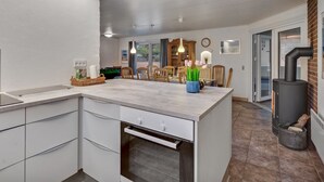 Une cuisine moderne dotée d’un îlot central, d’un four encastré et d’un coin repas avec des chaises et une table en bois.
