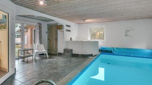 Une piscine avec un plafond en bois, une petite table et une chaise, dans une pièce dont le sol est carrelé.