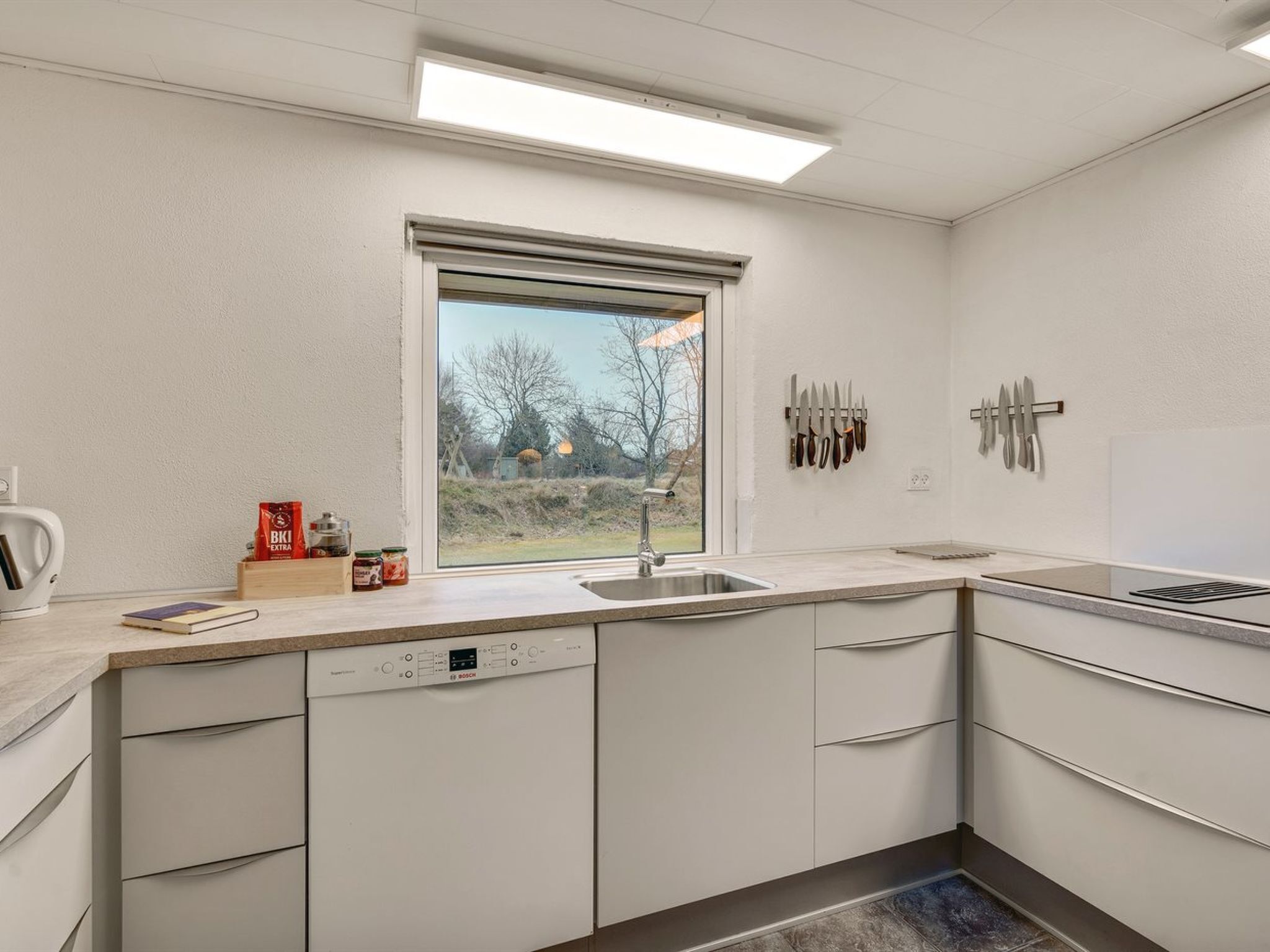 Une cuisine moderne équipée d’un lave-vaisselle Bosch, d’une fenêtre donnant sur l’extérieur et d’un porte-couteaux fixé au mur.