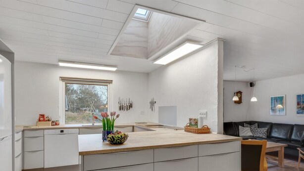 Une cuisine moderne avec un îlot central, un coin repas doté d’un canapé en cuir noir et une vue sur l’extérieur par une fenêtre.