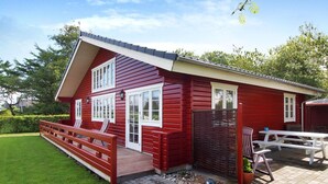 Una casa roja de madera con un porche, cerca de madera y una mesa de picnic.