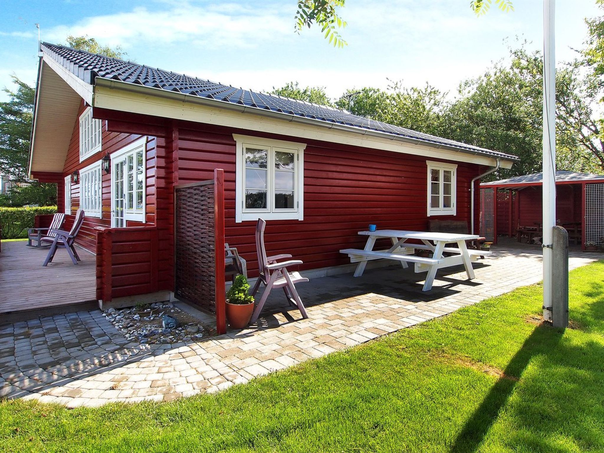 Une cabane en bois rouge avec une table de pique-nique et deux chaises à l’extérieur.
