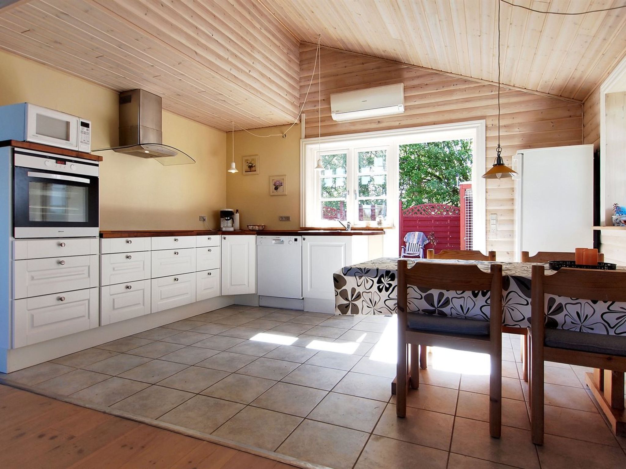 Una cocina con armarios blancos, microondas, horno y lavavajillas. Hay una mesa de comedor con sillas y una ventana con vistas al verde exterior.