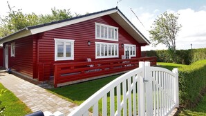 Una cabaña de madera roja con dos ventanas y un porche.