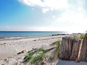 A sandy beach with a wooden post and some grass in the foreground.