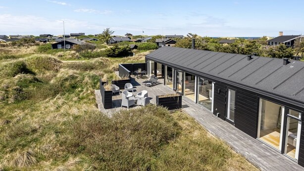 Una casa moderna con terraza, rodeada de dunas y otras viviendas.