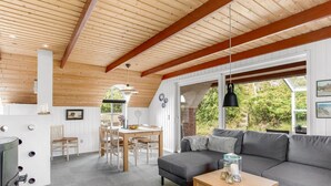 Una sala de estar acogedora con techo de madera, un sofá gris, una mesa de comedor con sillas y una chimenea.
