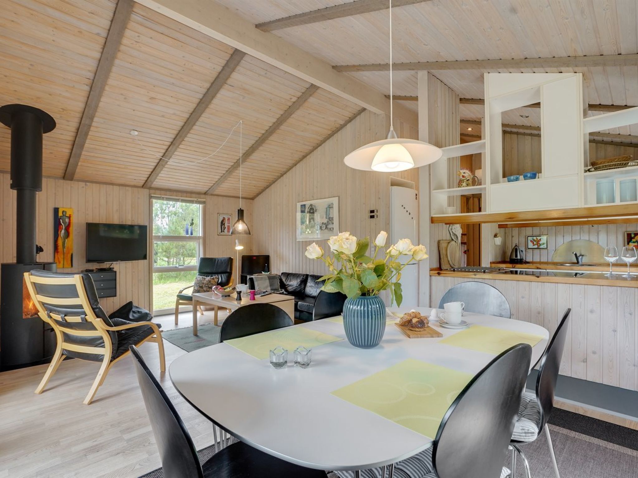 A modern kitchen with wooden cabinets, a dining area with a round table, and a living room with a fireplace.