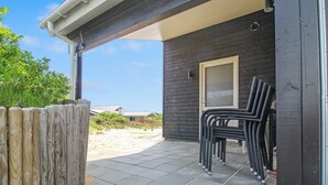 Un espacio al aire libre cubierto con un cerramiento de madera, un patio con baldosas y una puerta que da a un edificio de aspecto oscuro.